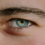 Detailed close-up image of a human eye with blue iris, capturing intricate details of the eyebrow and eyelashes.